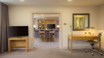 A hotel room with a TV, desk, chair, and a dining area with chairs and a table.