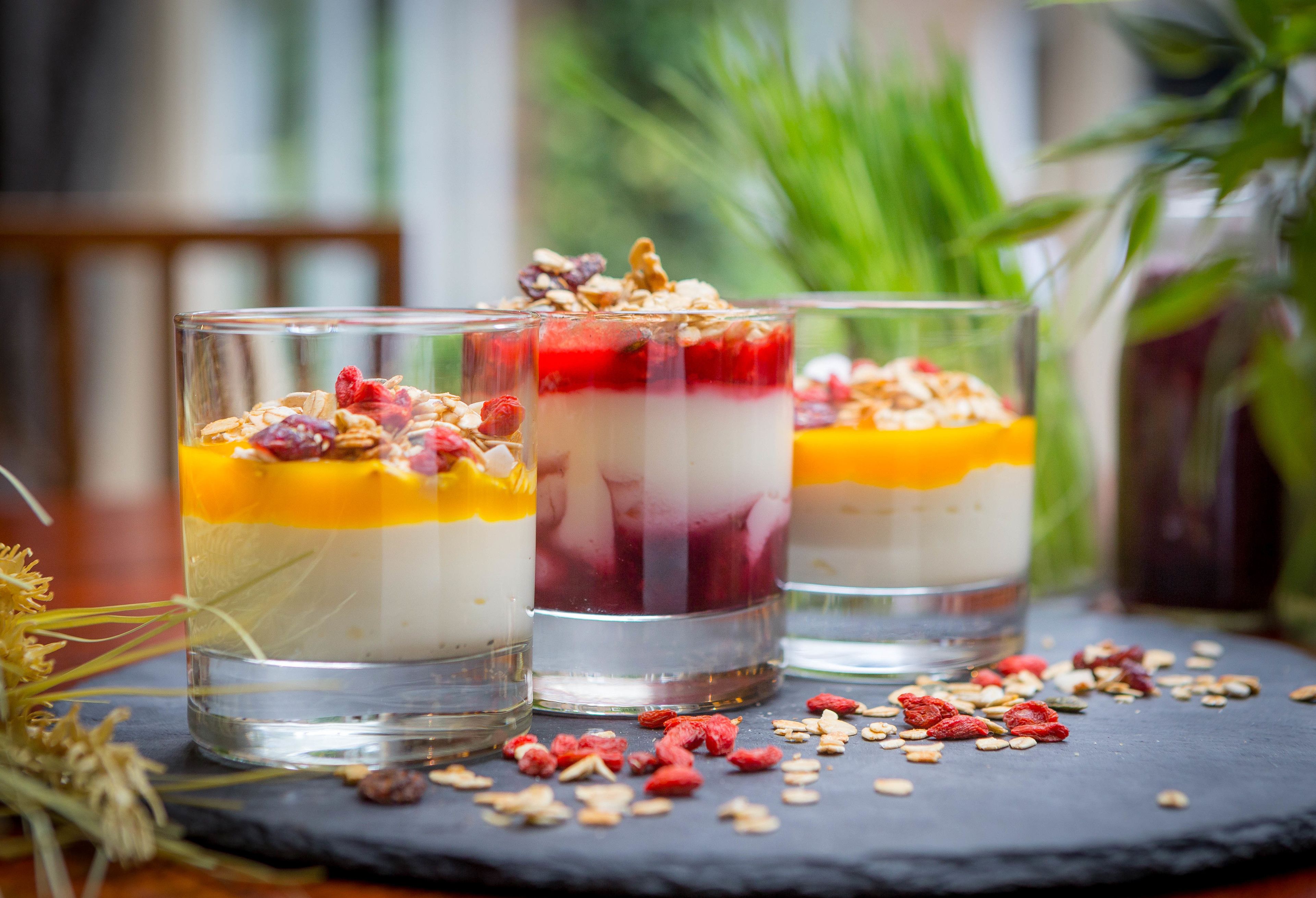 Tres copes de postre en capes sobre una taula de pissarra amb fruits secs i fruits dessecats dispersos.