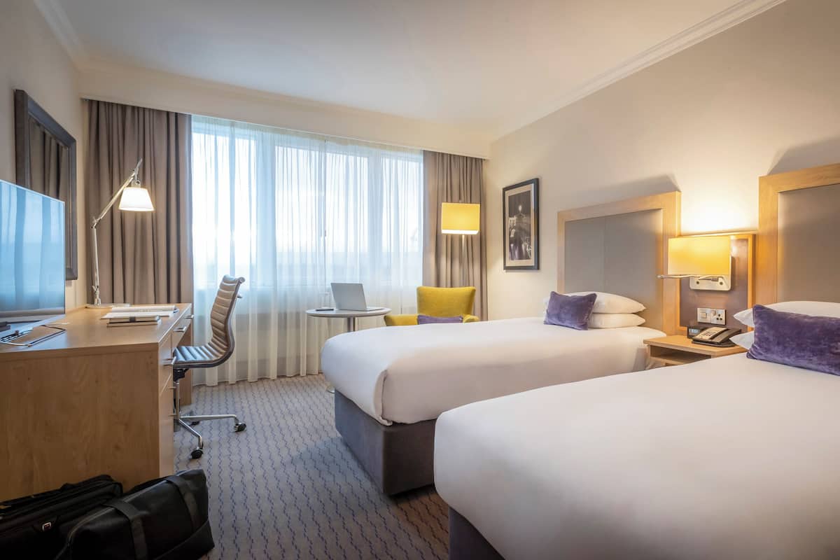 A hotel room with two beds, a desk, a chair, a laptop, and a telephone.