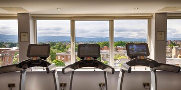 Three treadmills with screens, large windows, and a cityscape view.