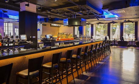 A bar area with a long counter, multiple taps, and bar stools.