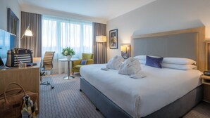 A hotel room with a large bed, a desk with a lamp, a chair, a small table with a plant, and a window with curtains. - Clayton Hotel Burlington Road (Dublin)