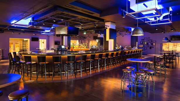 A modern bar area with a curved bar, multiple stools, and tables. - Clayton Hotel Burlington Road (Dublin)