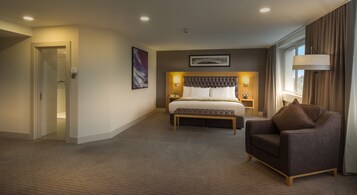 Habitación de hotel con una cama grande, una silla, una mesita de noche y una ventana con cortinas.
