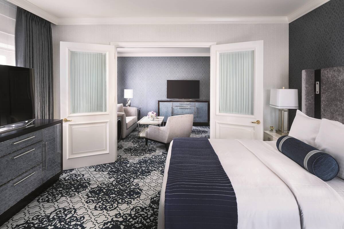 A hotel room with a large bed, a television, a desk with a lamp, and a chair.
