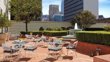 An outdoor patio with round tables and chairs, a fountain, and a view of city buildings.