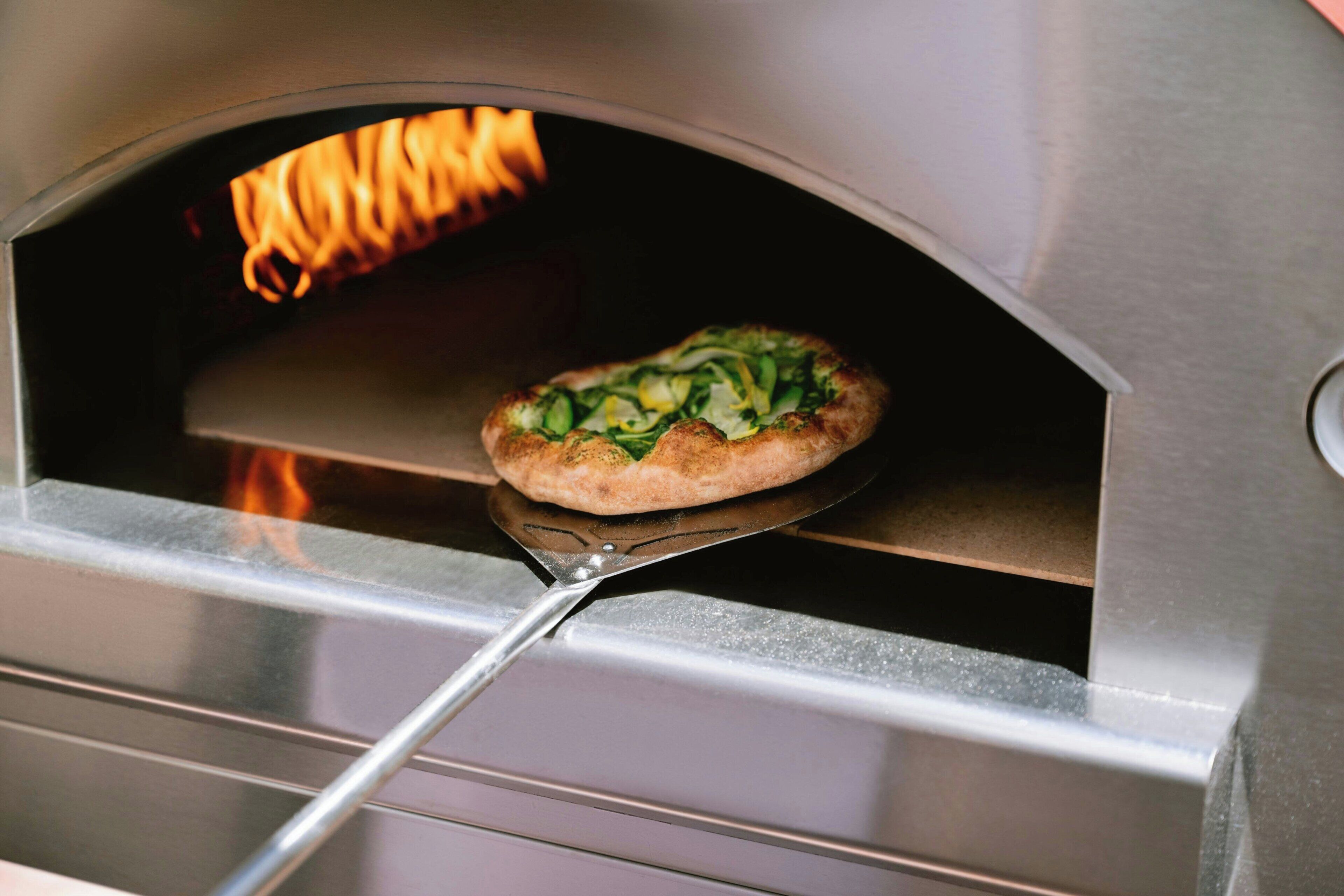 Une pizza à l’intérieur d’un four, avec une spatule à proximité.