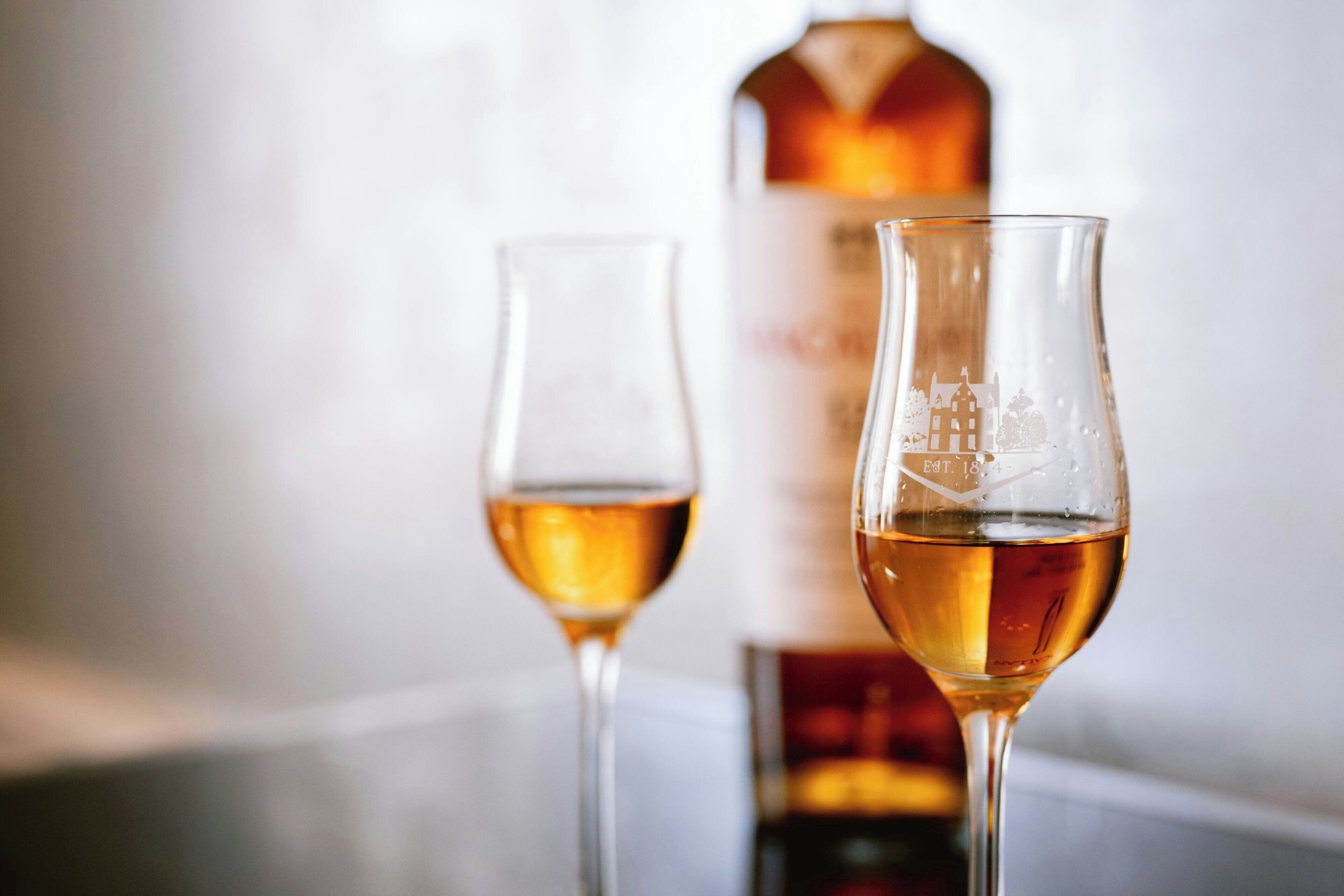 Two wine glasses with a bottle in the background.