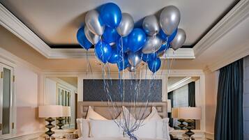 A hotel room with a large bed, two bedside tables with lamps, a mirror, and a ceiling with balloons.