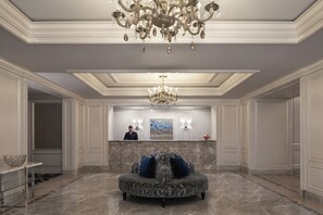A lobby with a round seating area, a chandelier, marble flooring, and a reception desk with a receptionist. - The Ritz-Carlton, San Francisco (San Francisco)
