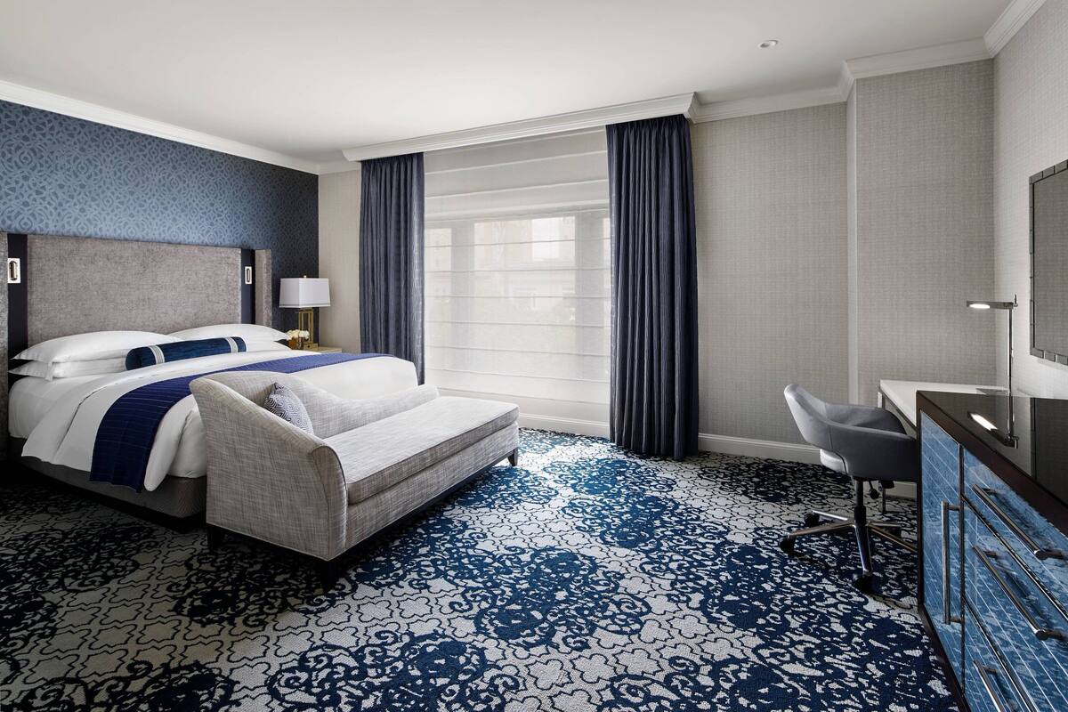 A hotel room with a large bed, a desk, a chair, and a window with curtains.