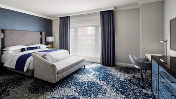 Una habitación de hotel con una cama, un escritorio, una silla y un ventanal con cortinas.