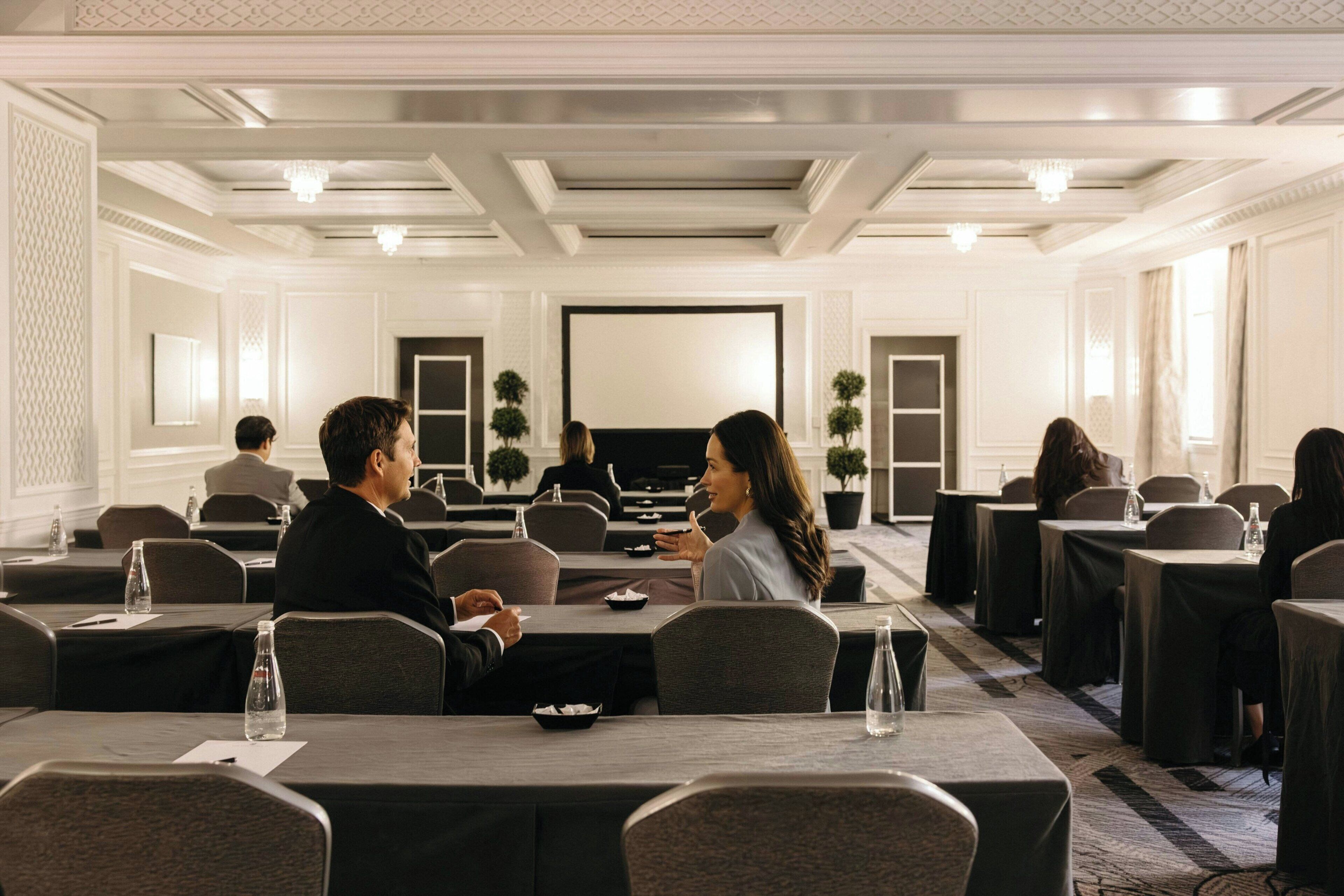 A conference room with tables, chairs, and a projector screen.