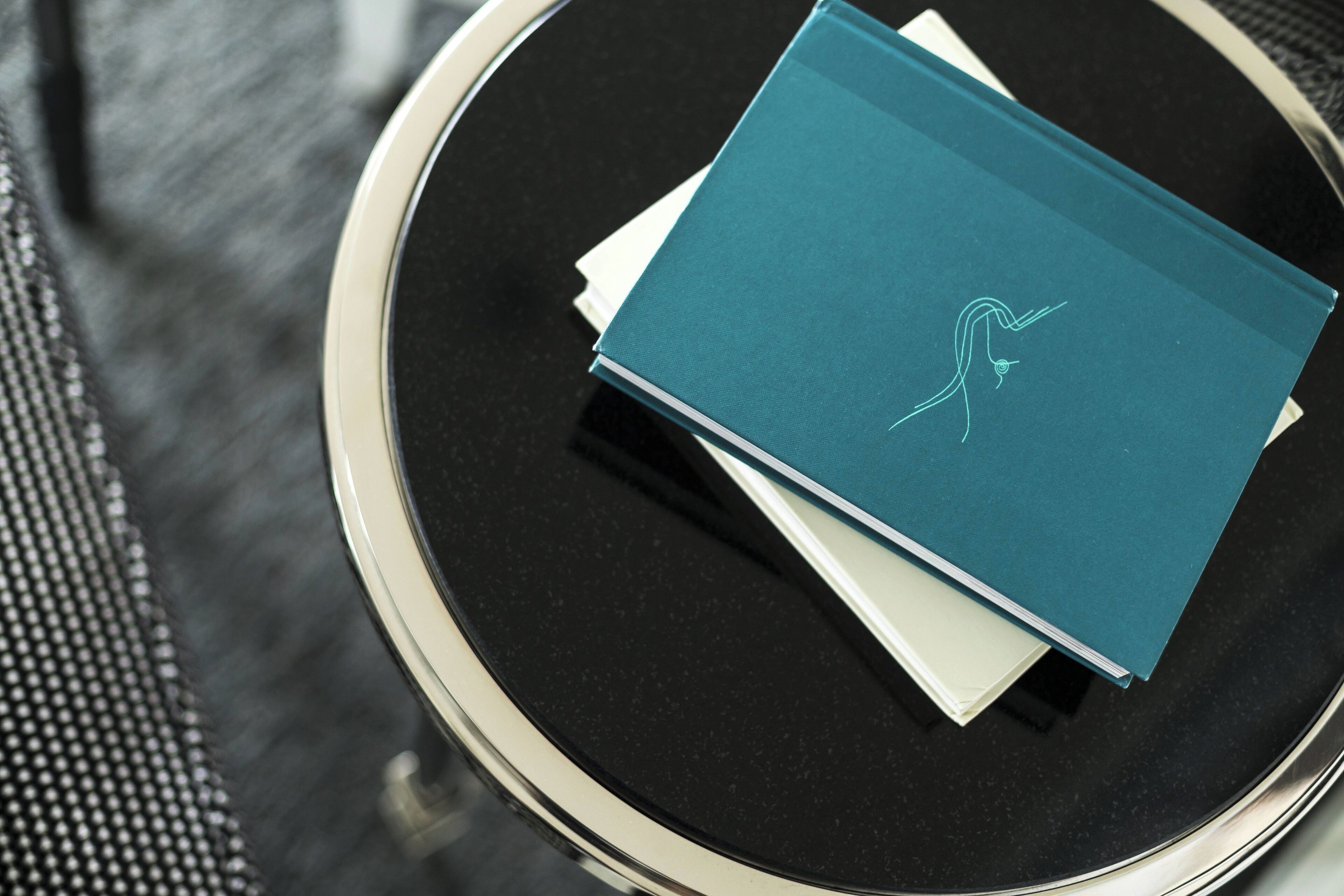 A teal book with a line drawing on the cover, placed on a round black table with a white napkin underneath.