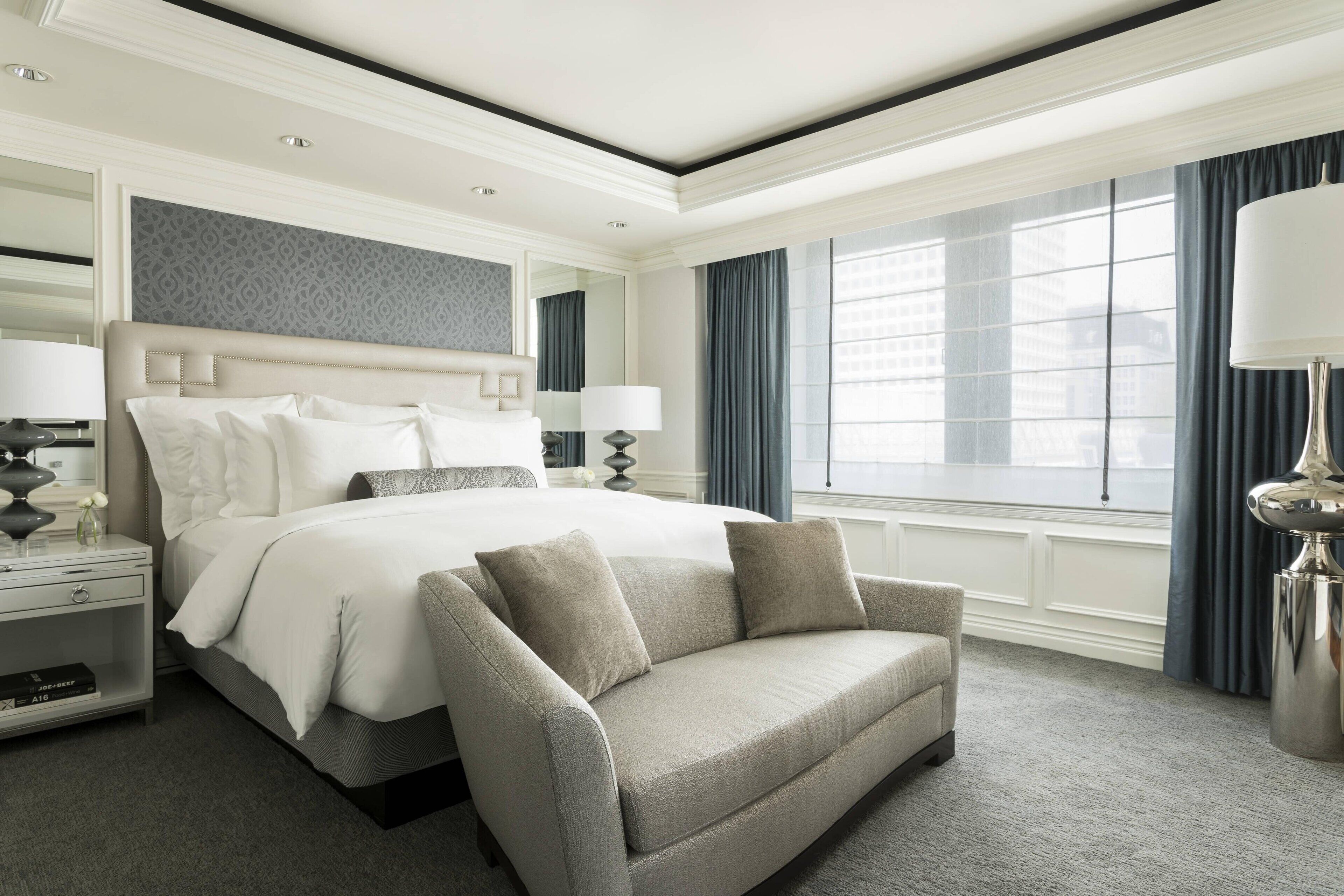 A hotel room with a large bed, a sofa, a nightstand, a lamp, and a window with curtains.