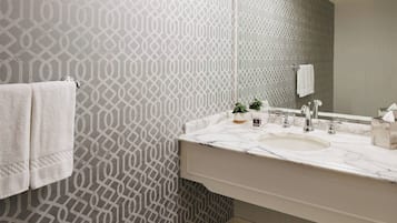 A bathroom with a patterned wallpaper, a white sink, a mirror, and a towel rack.