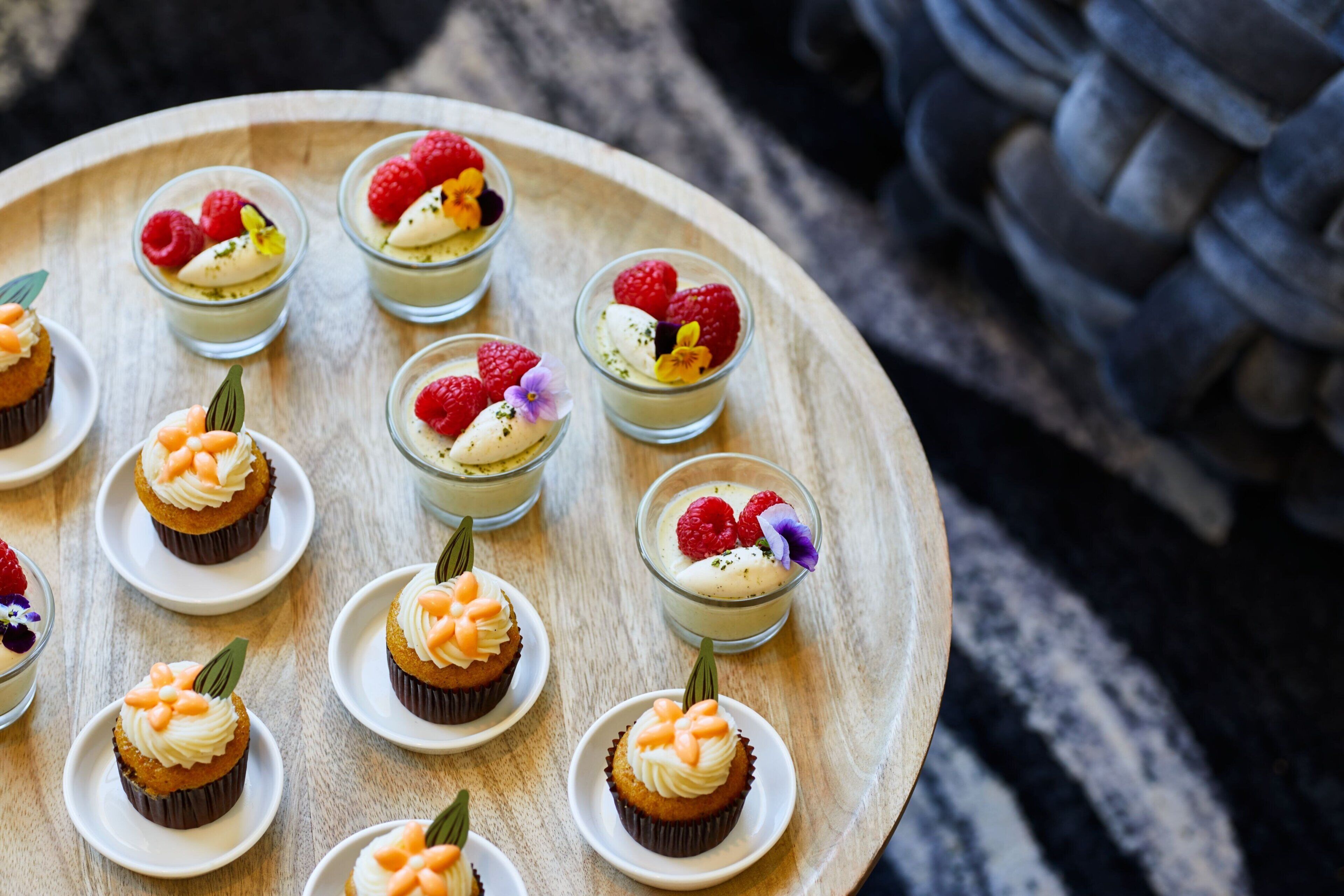 A wooden tray with cupcakes and small dessert cups, some with fruit toppings.