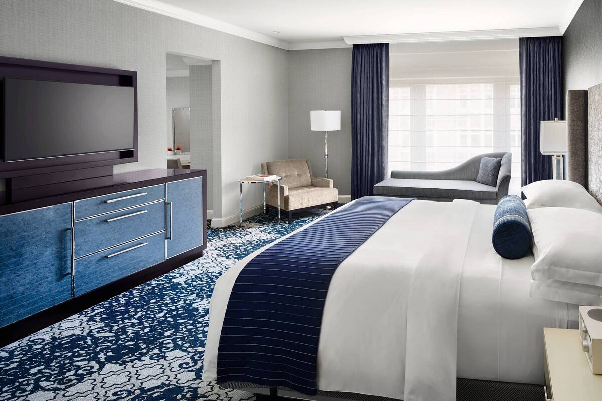 A hotel room with a large bed, a flat-screen TV, a desk, and a chair.