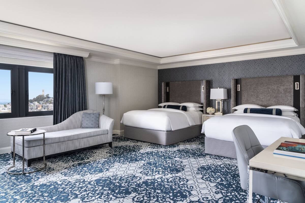 A hotel room with a large bed, a smaller sofa, a desk, and a view of a cityscape.