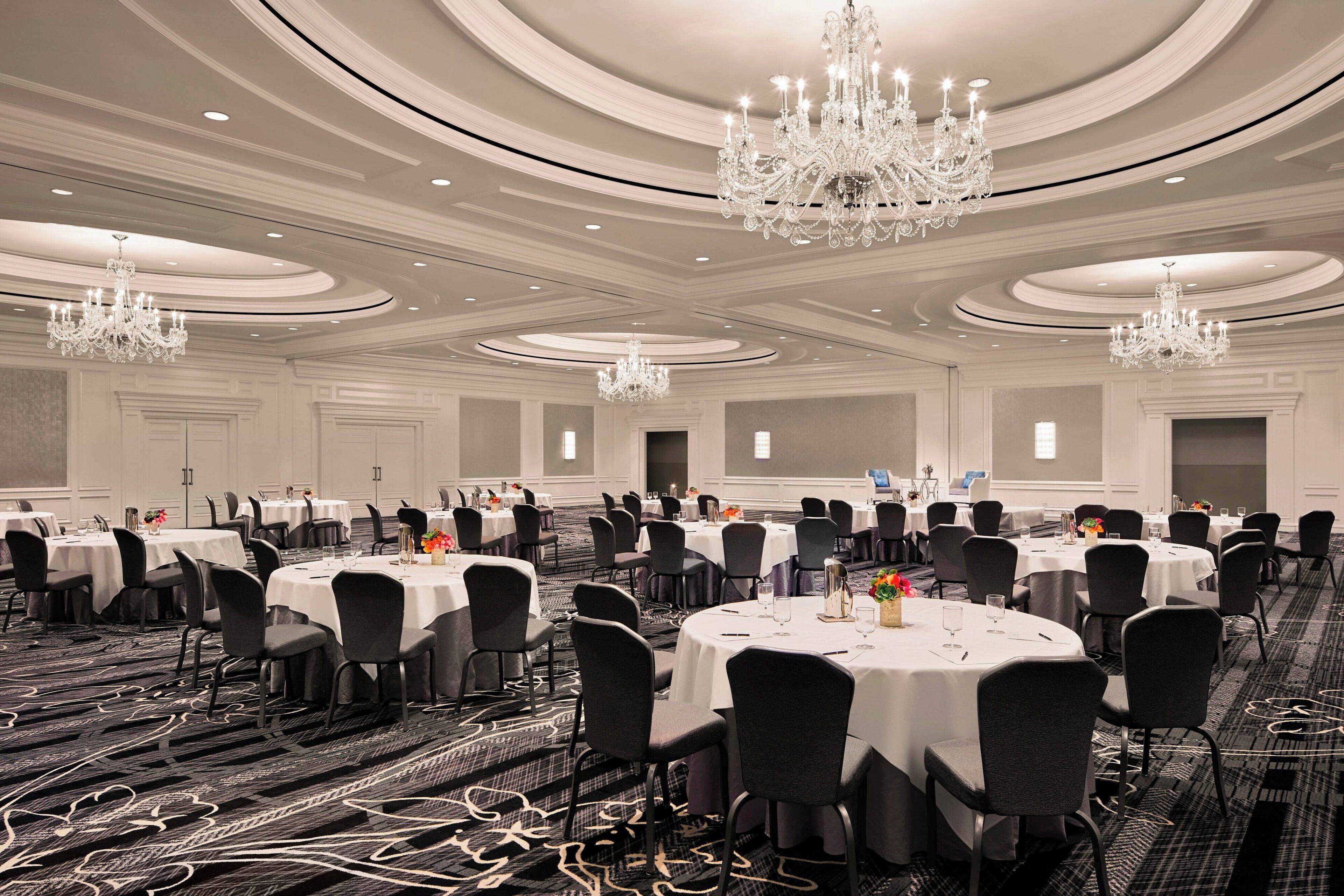 Un amplio salón de banquetes con varias mesas redondas, sillas negras y lujosos candelabros.