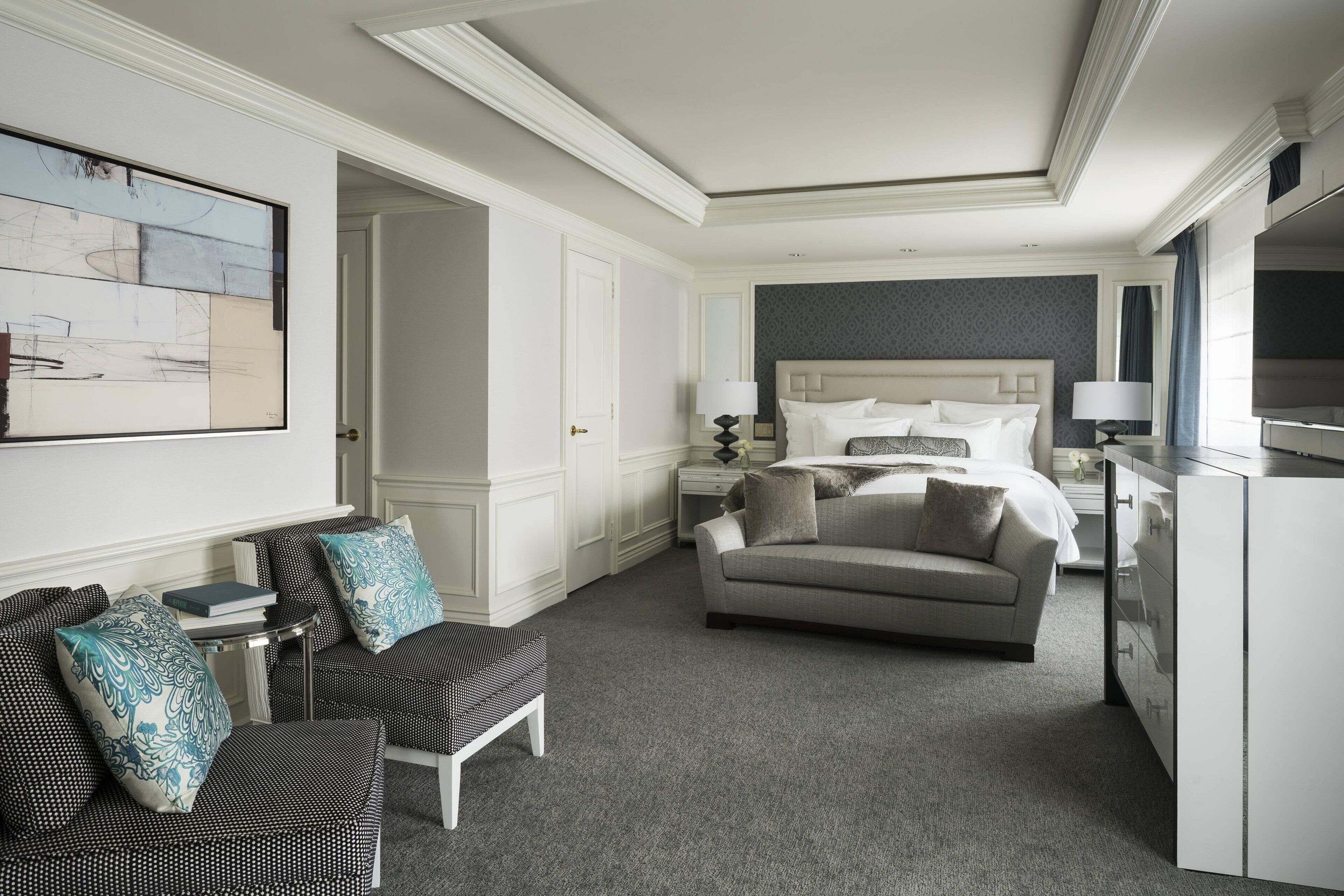 A hotel room with a bed, a chair, a desk, and a large painting on the wall.