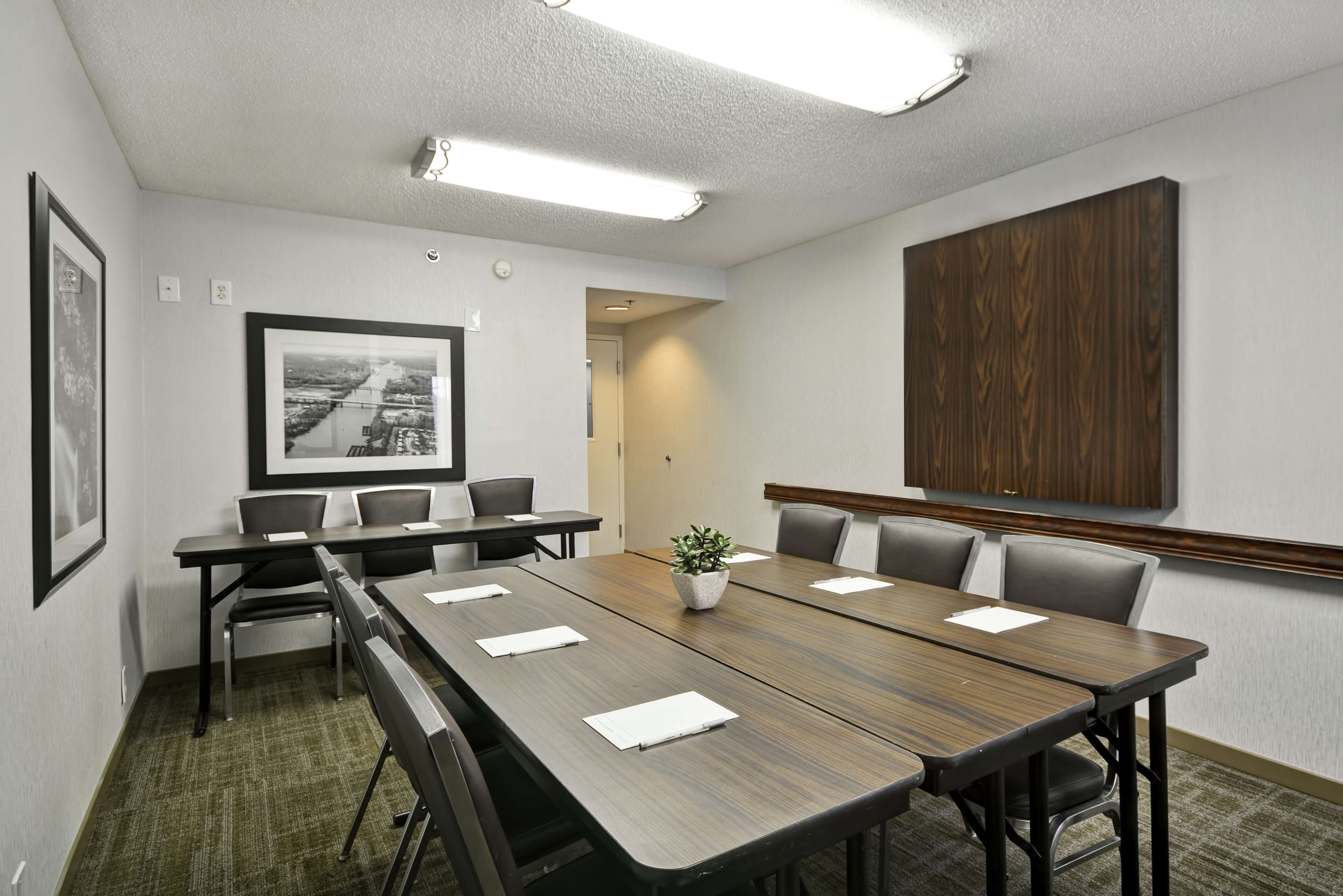 A conference room with a long table, chairs, framed pictures, and a wooden panel on the wall.