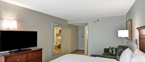 Una habitación de hotel con una cama, un televisor sobre una cómoda, un espejo y una puerta que da a un baño.