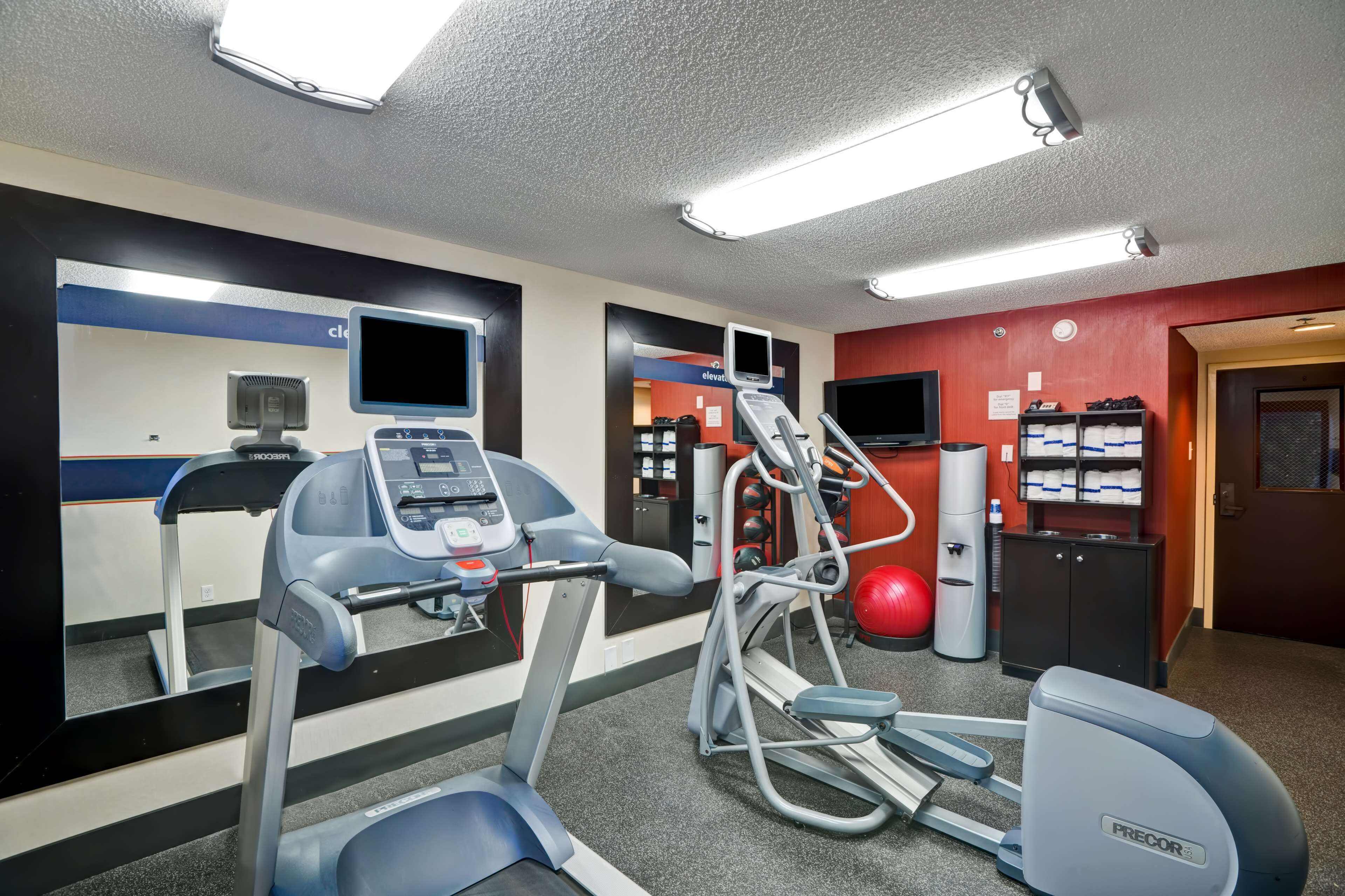 Een fitnessruimte met loopbanden, een elliptische trainer, een hometrainer en een rode fitnessbal.