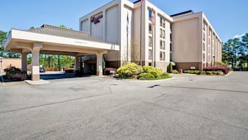 A Hampton Inn with a covered entrance, flag, and landscaped garden.