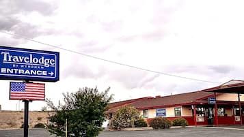 A Travelodge by Wyndham entrance sign, a parking lot, and a building with a red roof and beige walls.