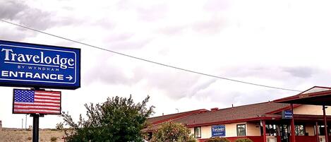 A Travelodge by Wyndham entrance sign, a parking lot, and a building with a red roof and beige walls.