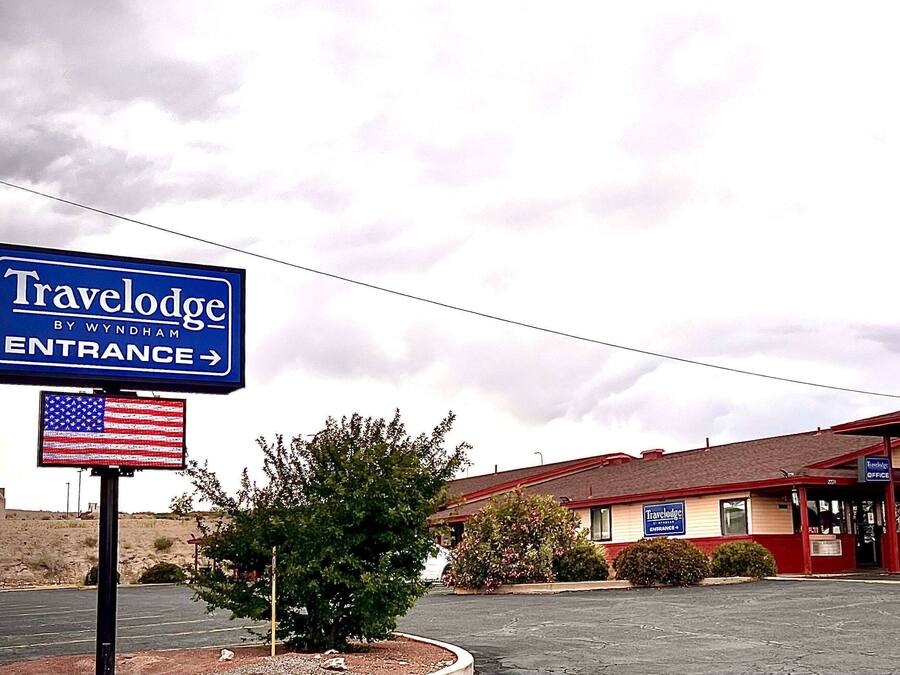 A Travelodge by Wyndham entrance sign, a parking lot, and a building with a red roof and beige walls.