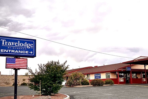 Señal de entrada de Travelodge by Wyndham, un estacionamiento y un edificio con techo rojo y paredes color crema.