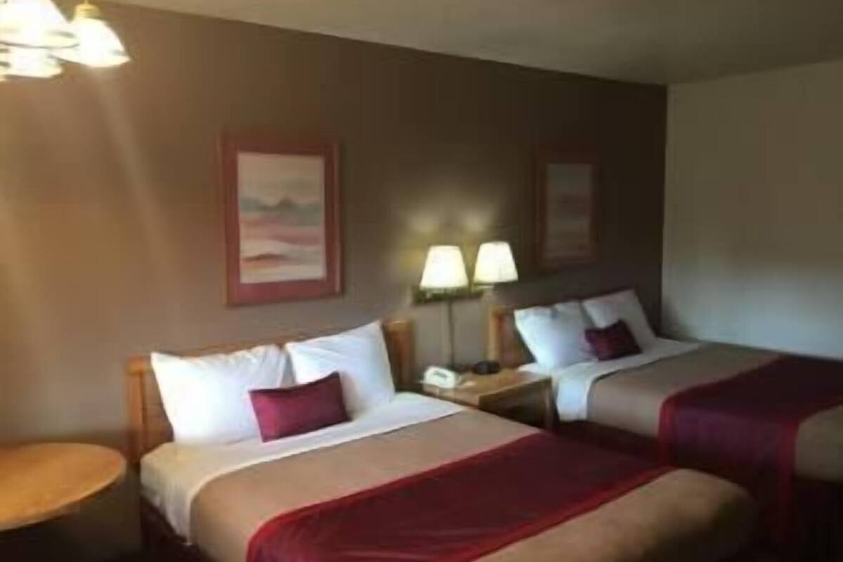 A hotel room with two beds, a small round table, and a nightstand with a lamp.