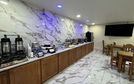 A hotel kitchen with marble countertops, coffee makers, a TV, and wooden cabinets.