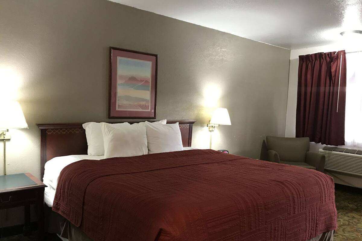 A hotel room with a large bed, two bedside lamps, a framed picture on the wall, a sofa, and a window with curtains.