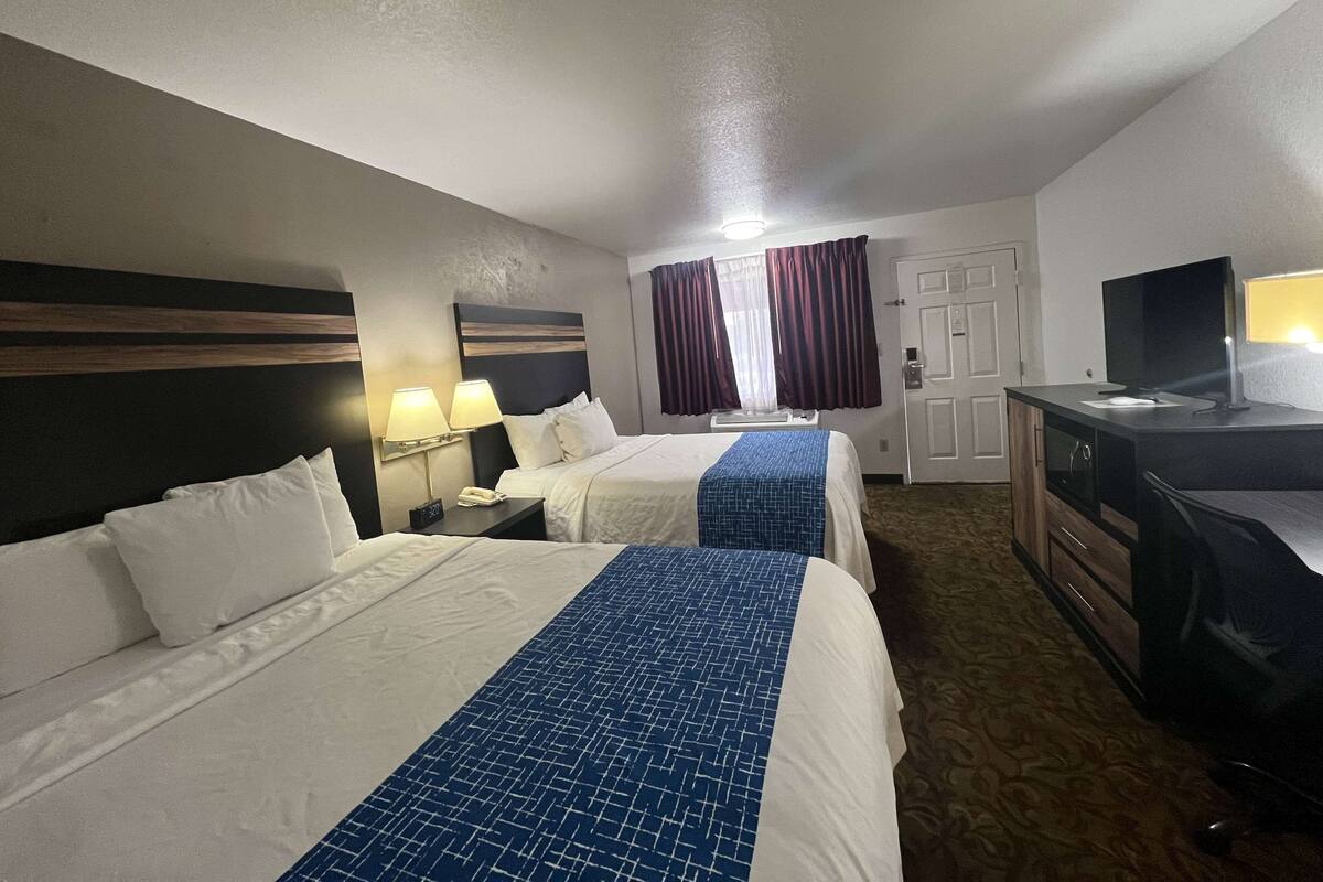A hotel room with two beds, a desk, a TV, and a window with curtains.