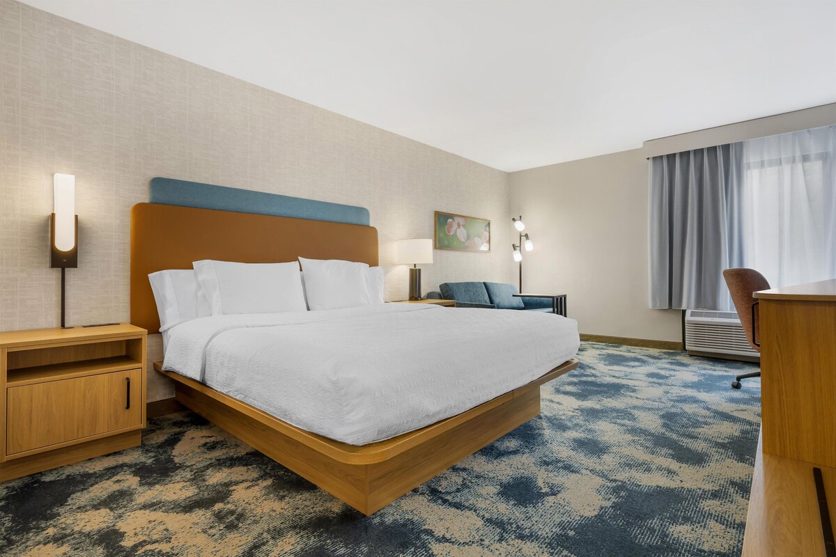 A hotel room with a large bed, bedside tables, a desk, a chair, and a window with curtains.