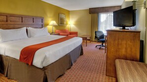 A hotel room with a large bed, a desk, a chair, and a television.