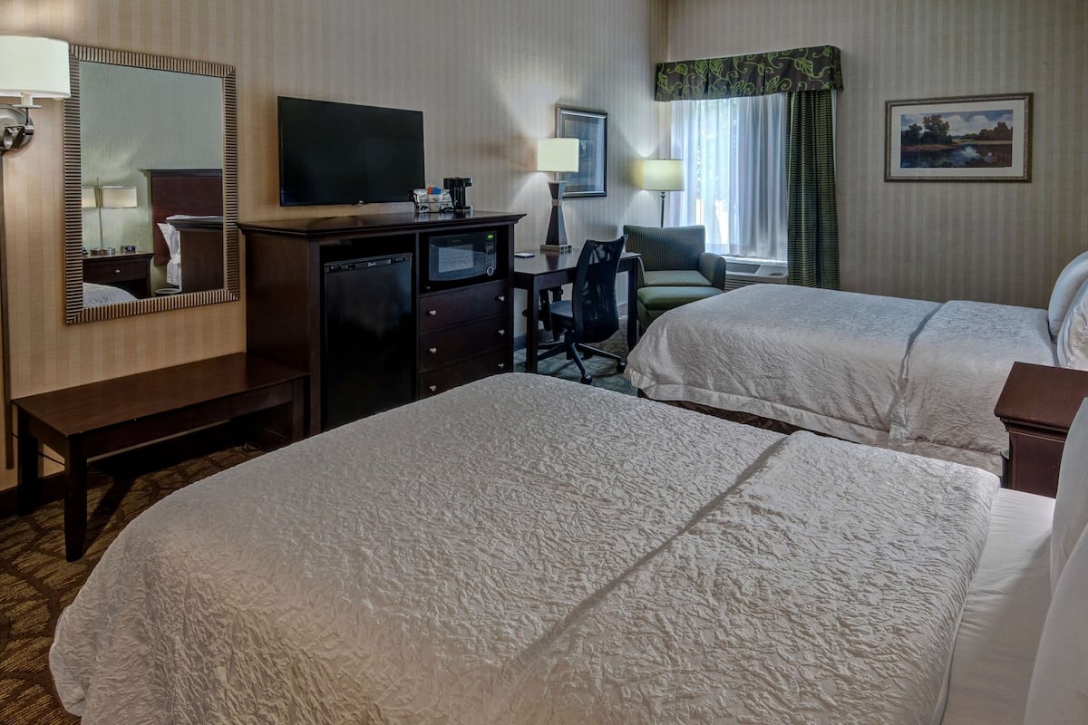 Een hotelkamer met twee bedden, een bureau met een computer, een televisie en een spiegel.