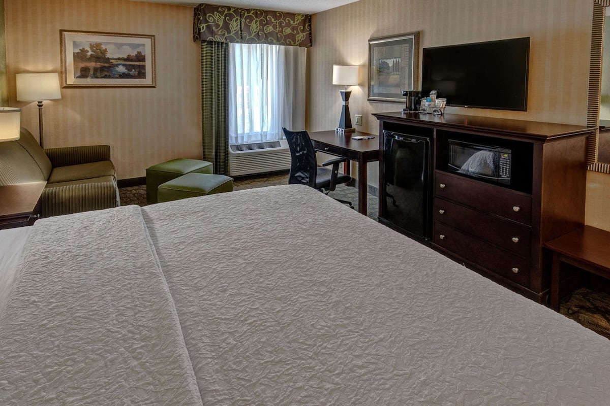Hotelkamer met een groot bed, een bureau met stoel, een televisie, een magnetron en een klein tafeltje met lamp.