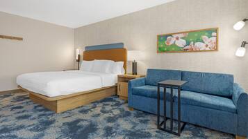 Ein Hotelzimmer mit einem Bett, einem blauen Sofa, einem kleinen Tisch und einem Bild an der Wand.