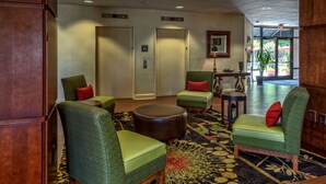 A lobby with green upholstered chairs, a round leather ottoman, and a patterned carpet.