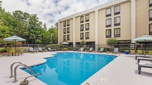 A swimming pool with lounge chairs and umbrellas, surrounded by a building with multiple windows.