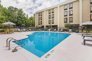 A swimming pool with lounge chairs and umbrellas, surrounded by a building with multiple windows.
