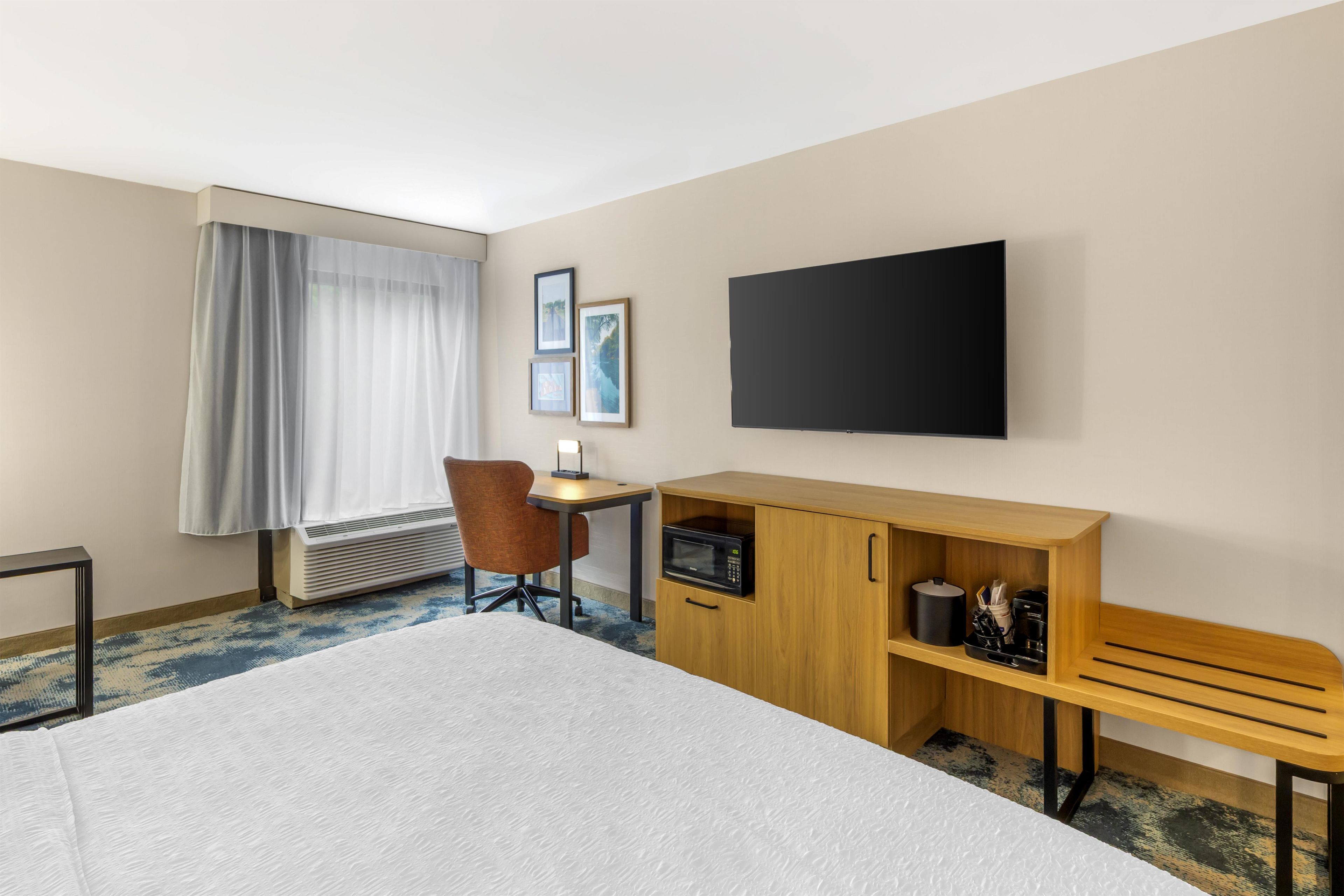 A hotel room with a bed, a desk, a chair, a flat-screen TV, and a wooden cabinet.