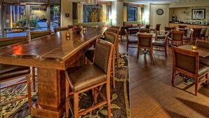 A spacious hotel dining area with a long wooden table, multiple chairs, and a separate seating area with cushioned benches.