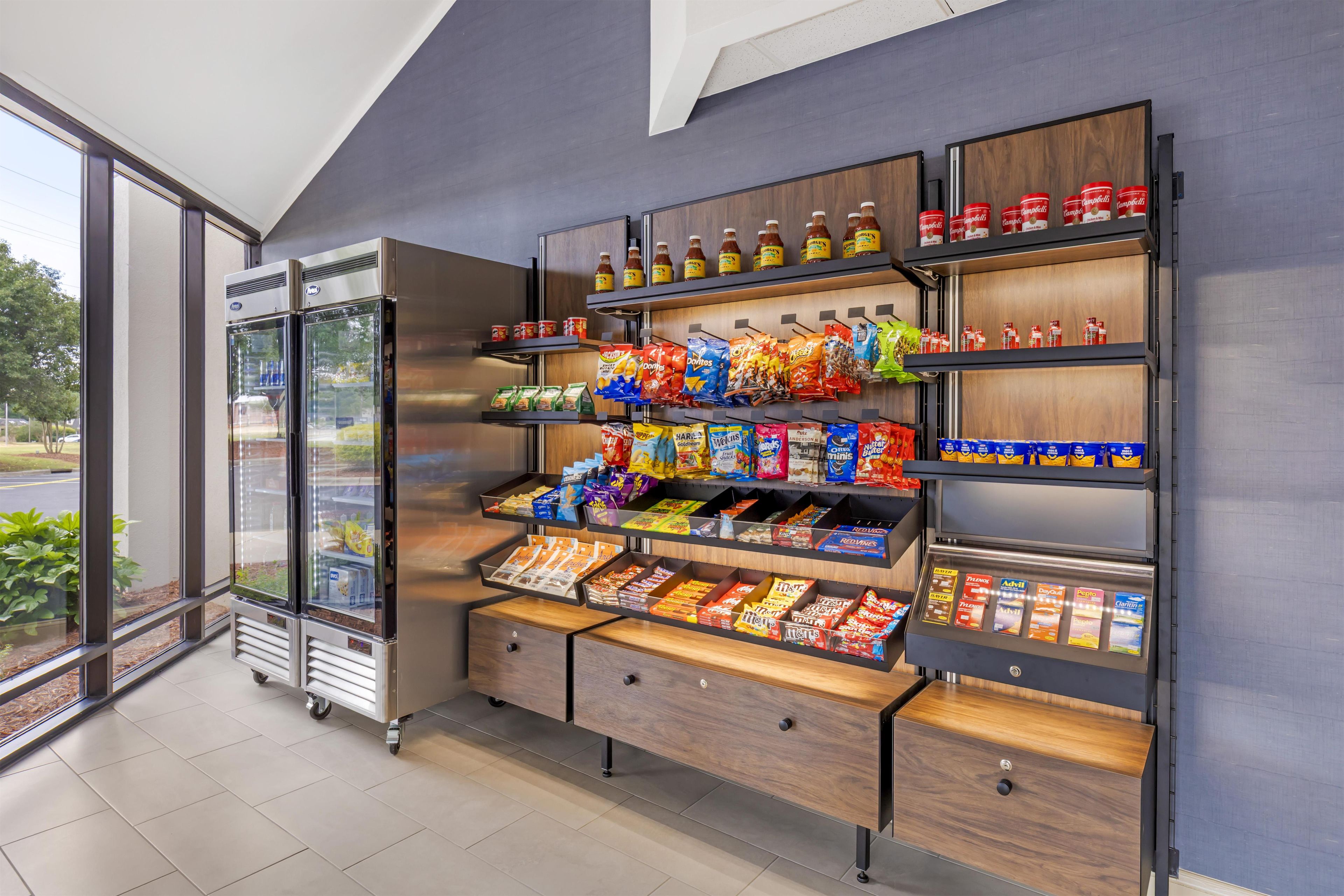 A vending machine with snacks and drinks, a refrigerated display case, and a wooden shelf unit with various packaged goods.