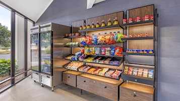 A vending machine with snacks and drinks, a refrigerated display case, and a wooden shelf unit with various packaged goods.