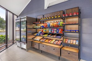 A vending machine with snacks and drinks, a refrigerated display case, and a wooden shelf unit with various packaged goods.